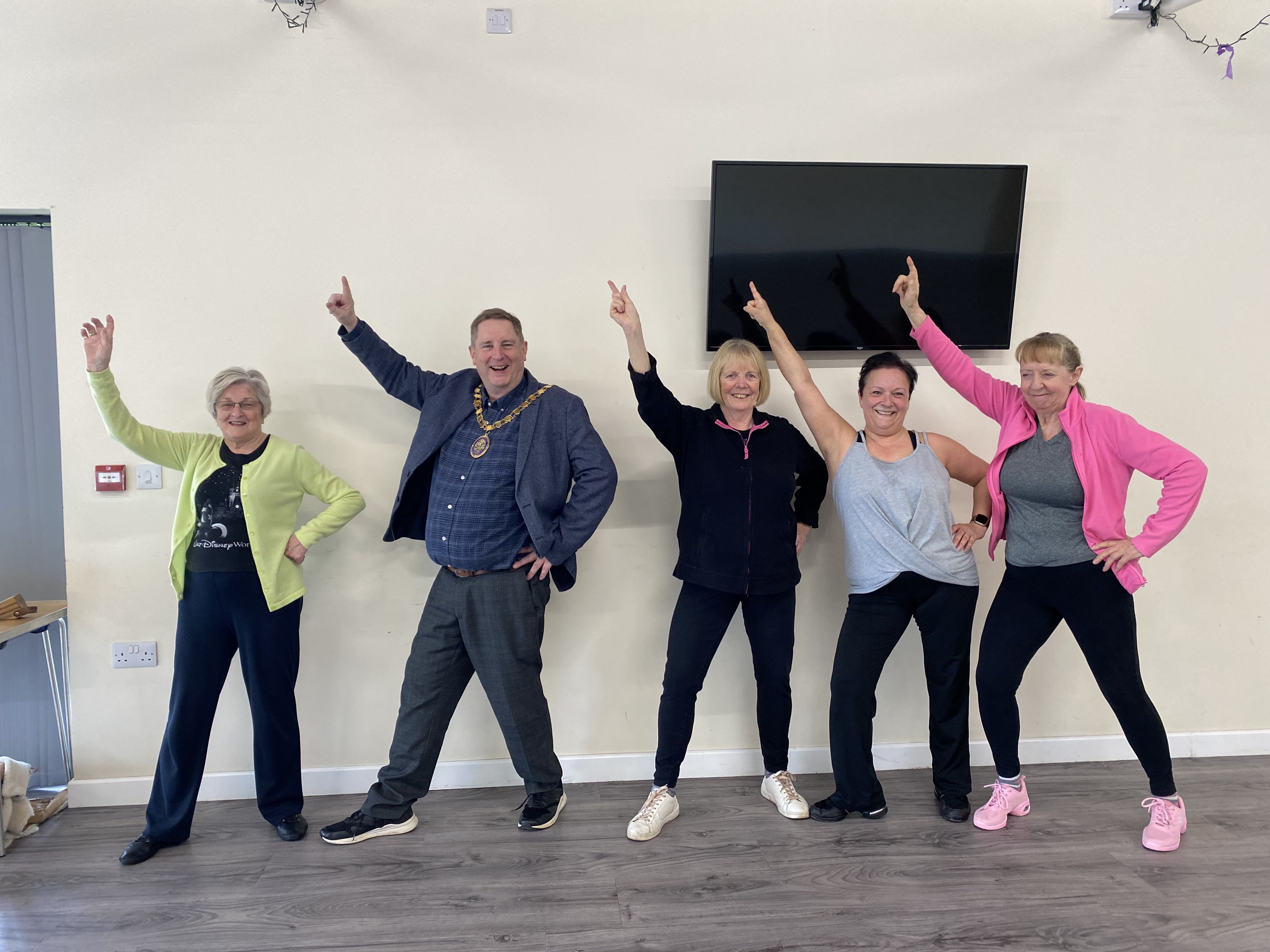 Five people stood against a wall doing a dance pose.
