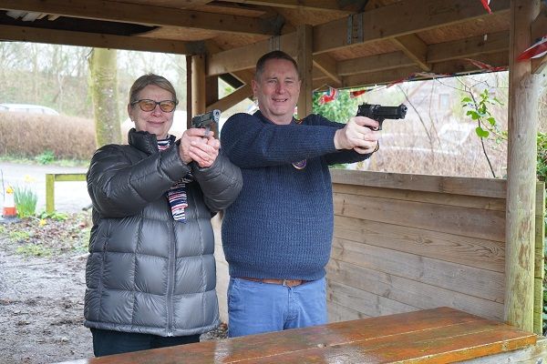 A woman and a man standing side by side holding air pistols pointing at the camera.