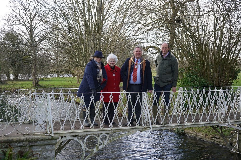 Four people stood on an iron lattice bridge with trees in the background.