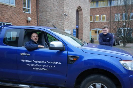 Jack Williams peering out of a car window with Joe Jones leant over the front.