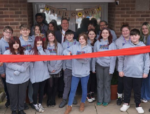 A group of people stood in front of a red ribbon ready to cut it