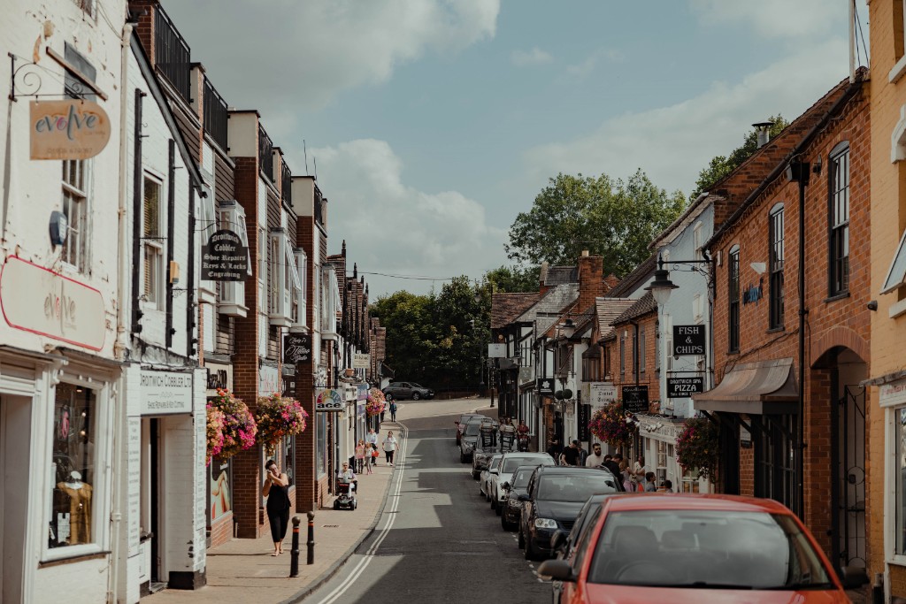Droitwich High Street with shops on the left a road down the middle and parked cars on the right.