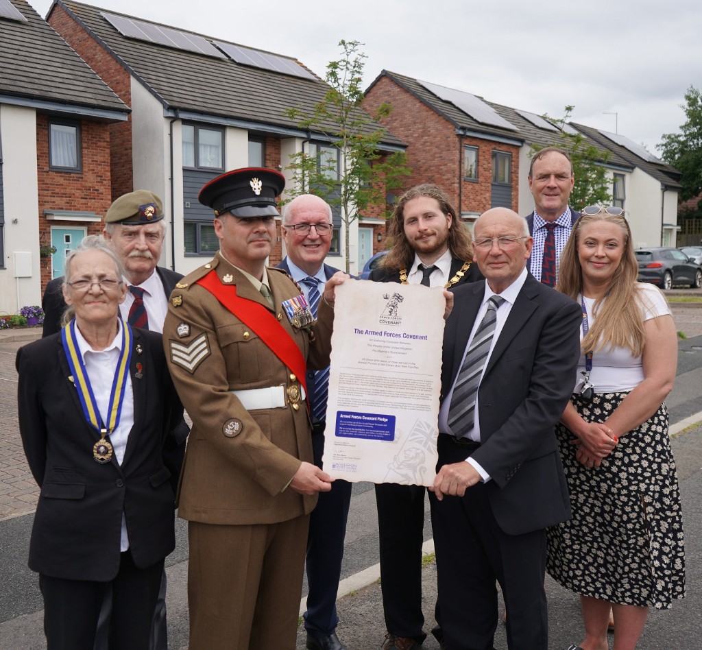 A group of people holding a scroll stood in front of some houses.