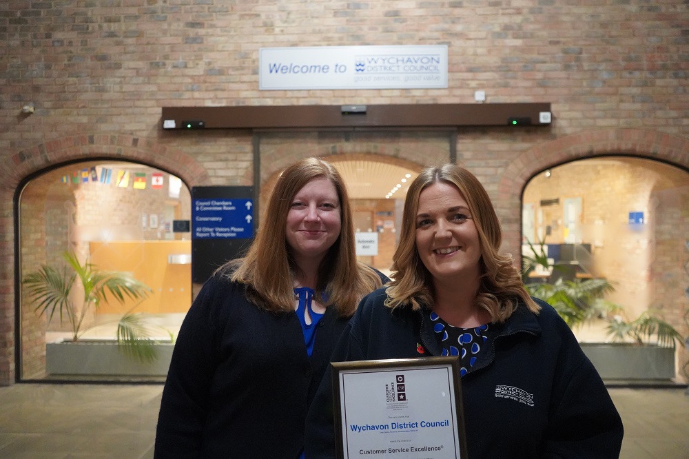 Two women holding a certificate stood in front of an entrance