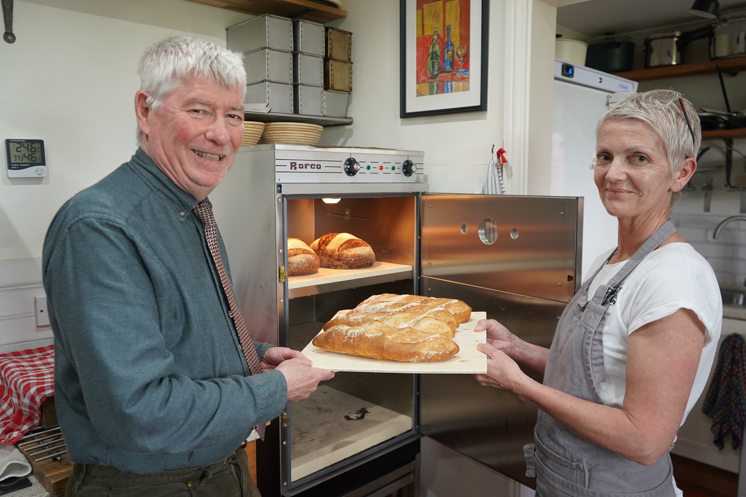 Two people holding a tray of bread in front of a baking oven