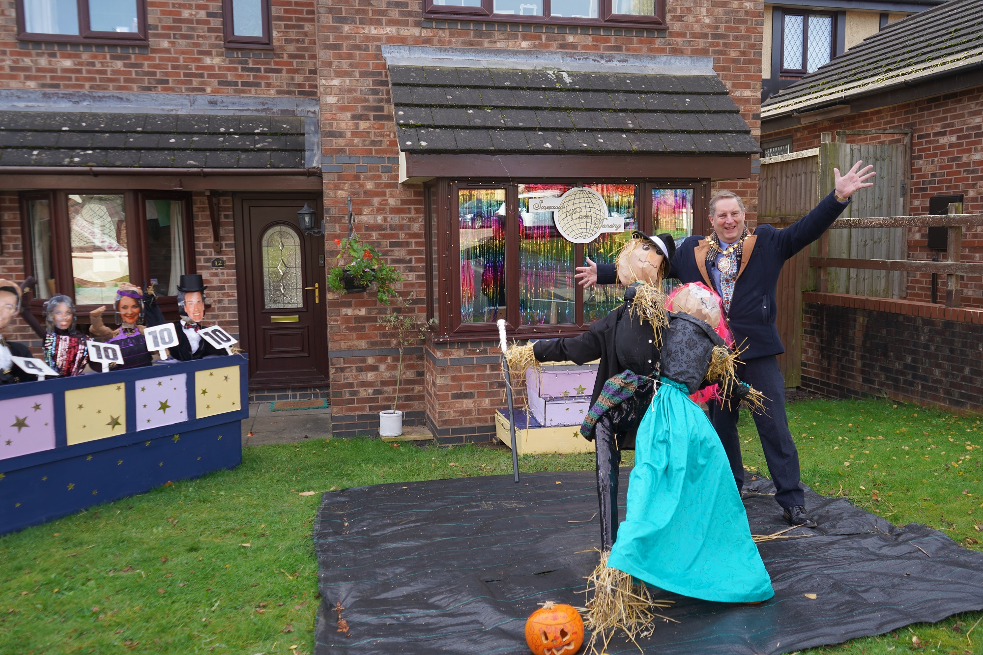 A man stood in a dance pose in front of a group of scarecrows made up to look like dancers and judges from Strictly Come Dancing.