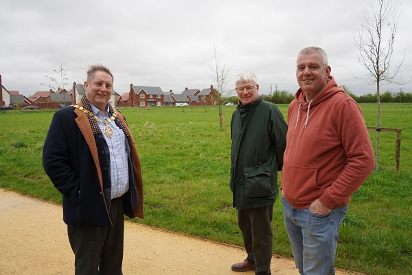Three men stood on a path in front of a field.