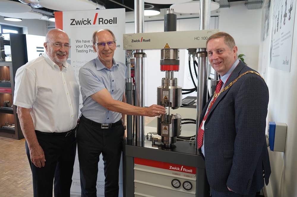 Three men stood in front of a testing machine.