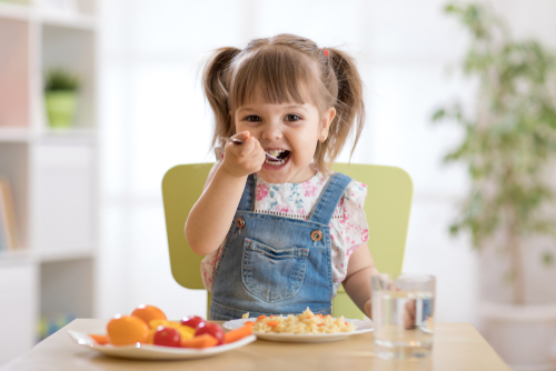 A little girl eating healthy food staring at the camera.