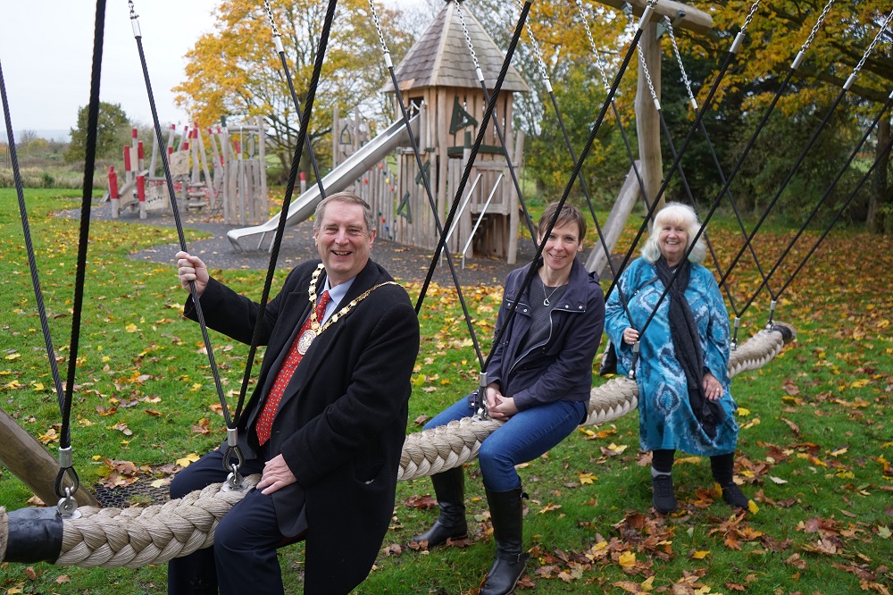 Three people sat on a rope swing in a park.