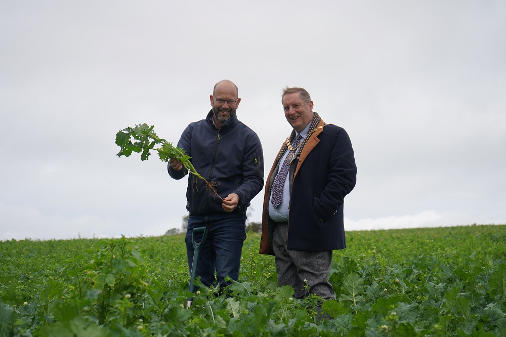 Two men stood in a field holding a plant.