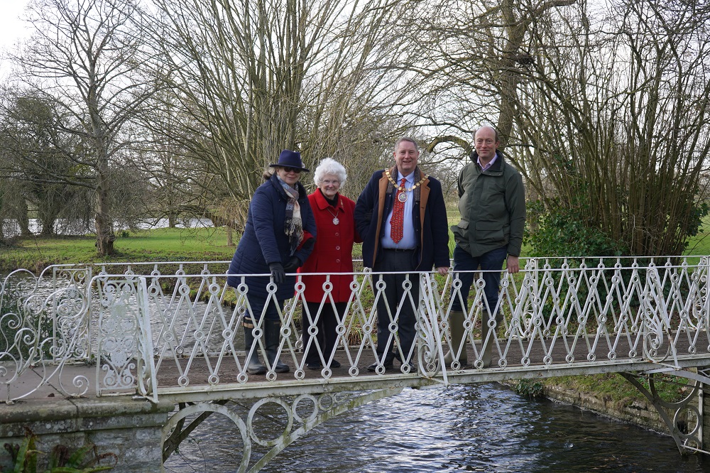 Four people stood on an iron lattice bridge with trees in the background.