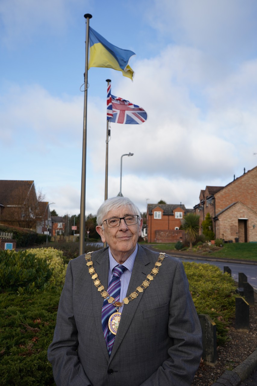 A man stood in front of two flag poles with the Ukraine flag and Union flag flying above his head.